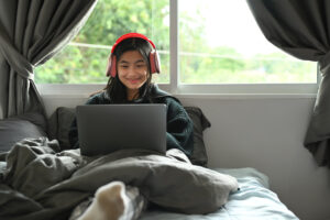 Teenage girl wearing headphone, virtual remote e learning on laptop in bedroom. Distance education, studying online concept